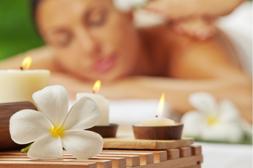 woman enjoying a massage with three lit flowers and flower petals